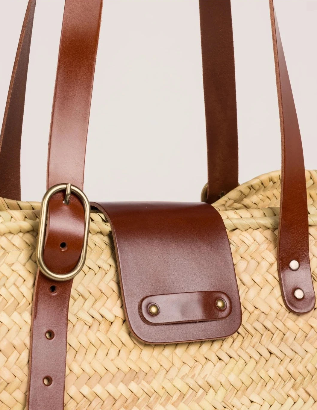 Close-up of Aicha basket bag showing dark brown calfskin leather flap, buckle, and woven palm leaf texture
