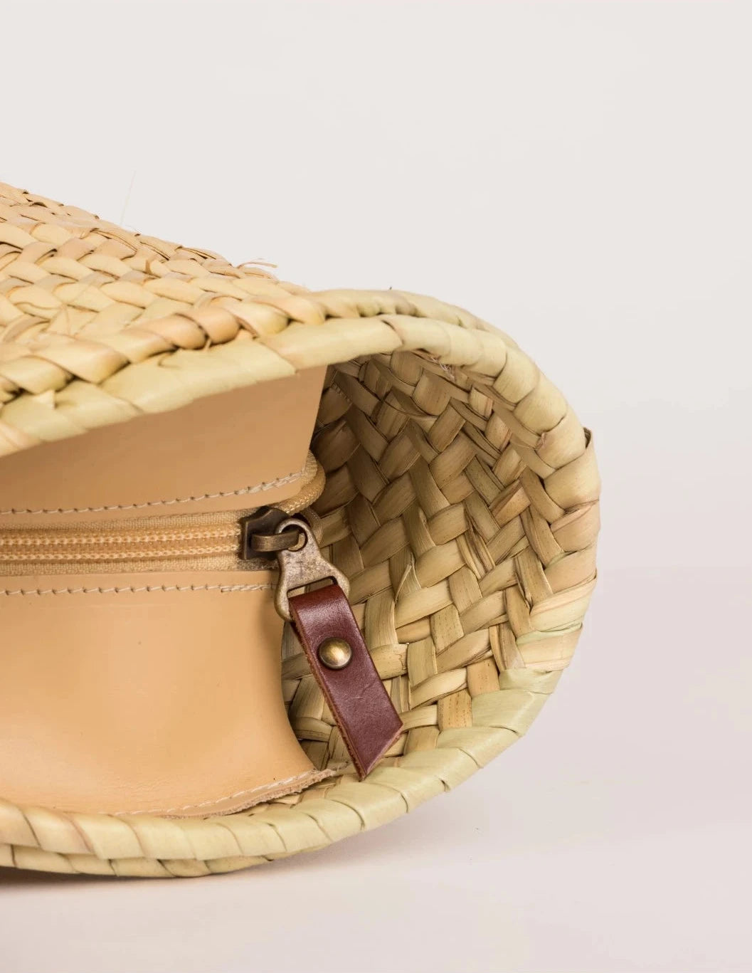 Interior view of Aicha palm leaf basket bag with zip closure and dark brown leather trim