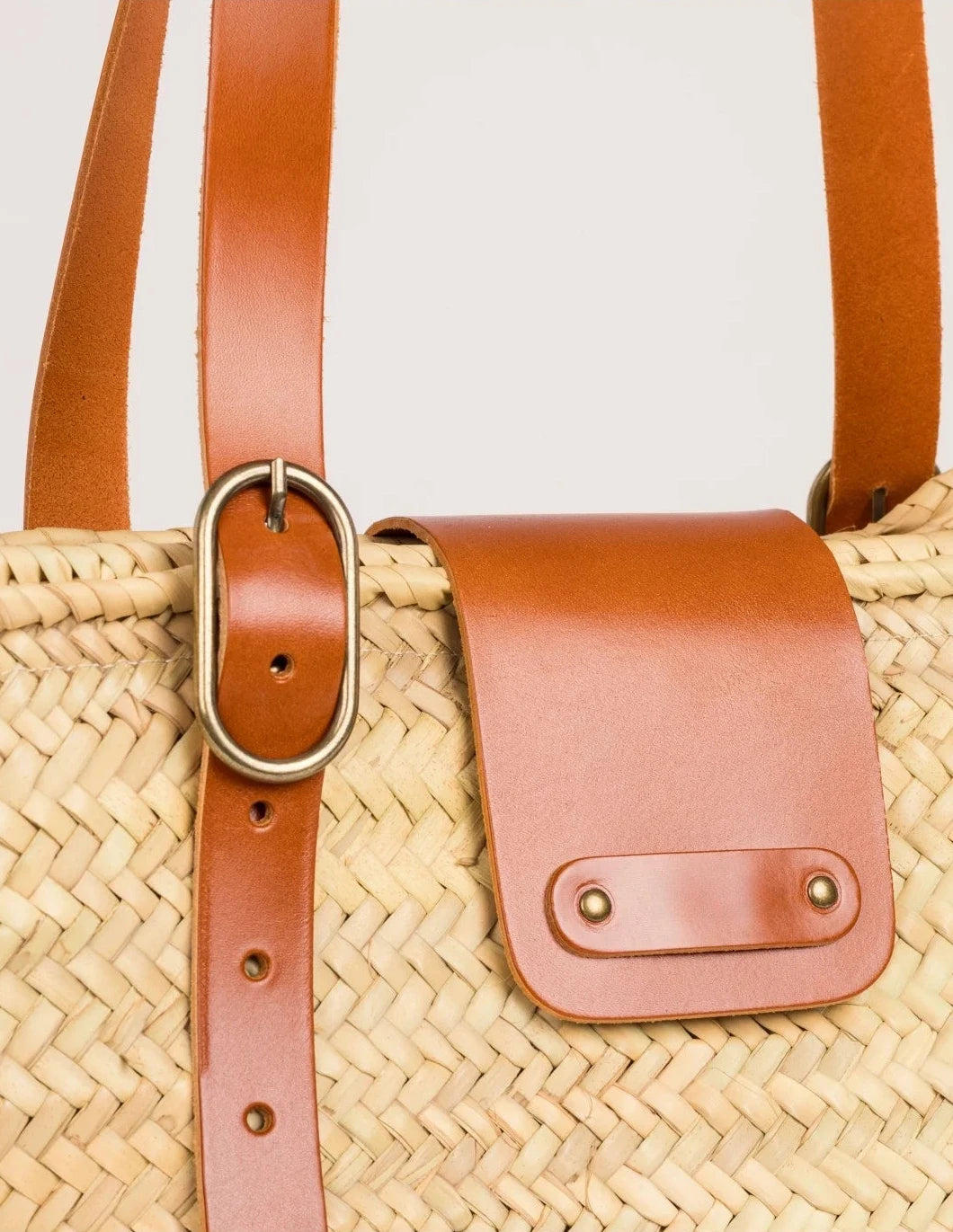Close-up of Aicha basket bag showing light brown calfskin leather flap, buckle, and woven palm leaf texture