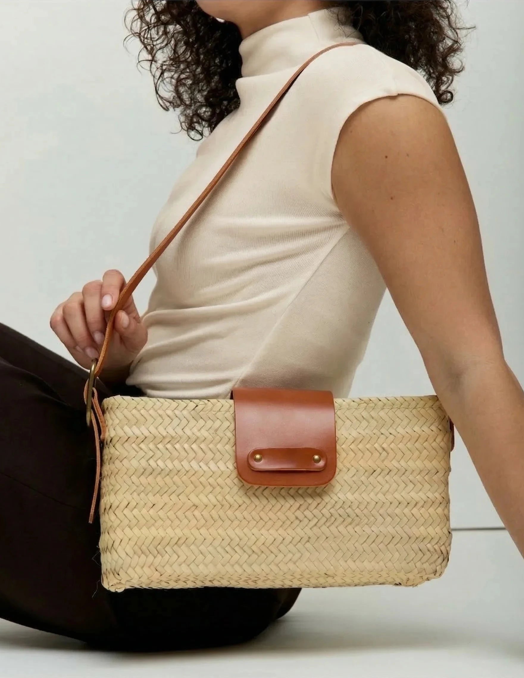Model seated, carrying the Asmae palm leaf baguette bag with light brown calfskin strap