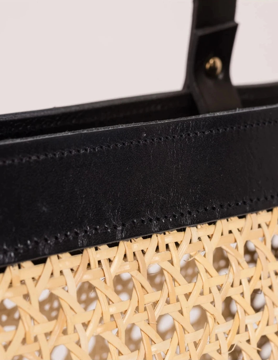 Close-up of the black calfskin handles and leather frame on the Lamia Cane Tote