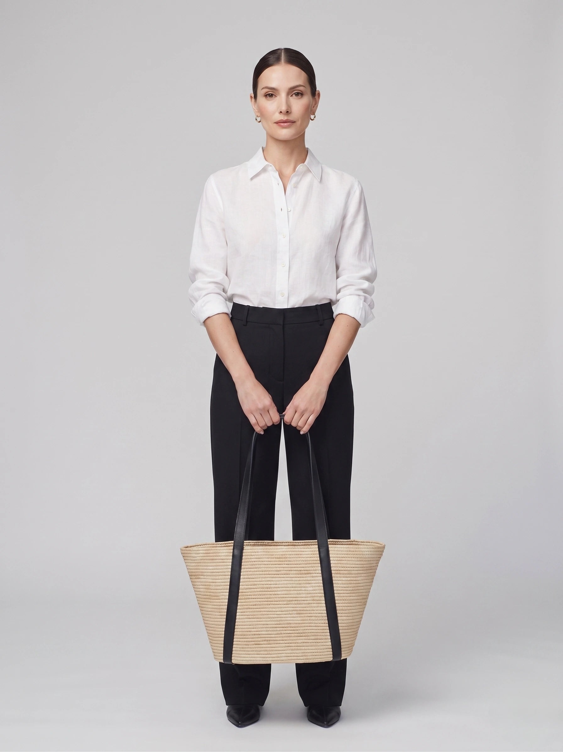 Model holding the Kenza raffia basket tote with black straps, front view