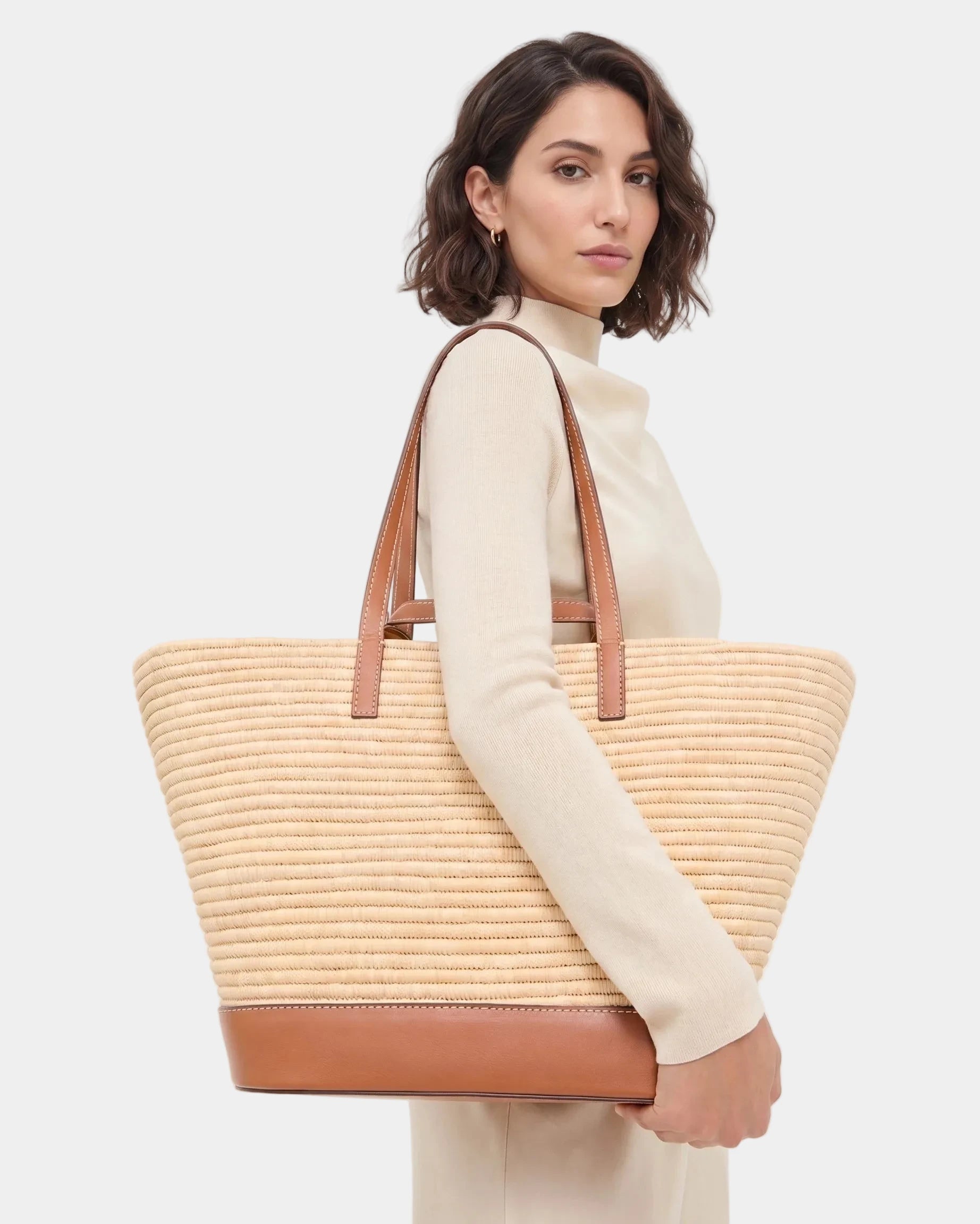 Woman in cream carrying the Najwa raffia basket tote on her shoulder.