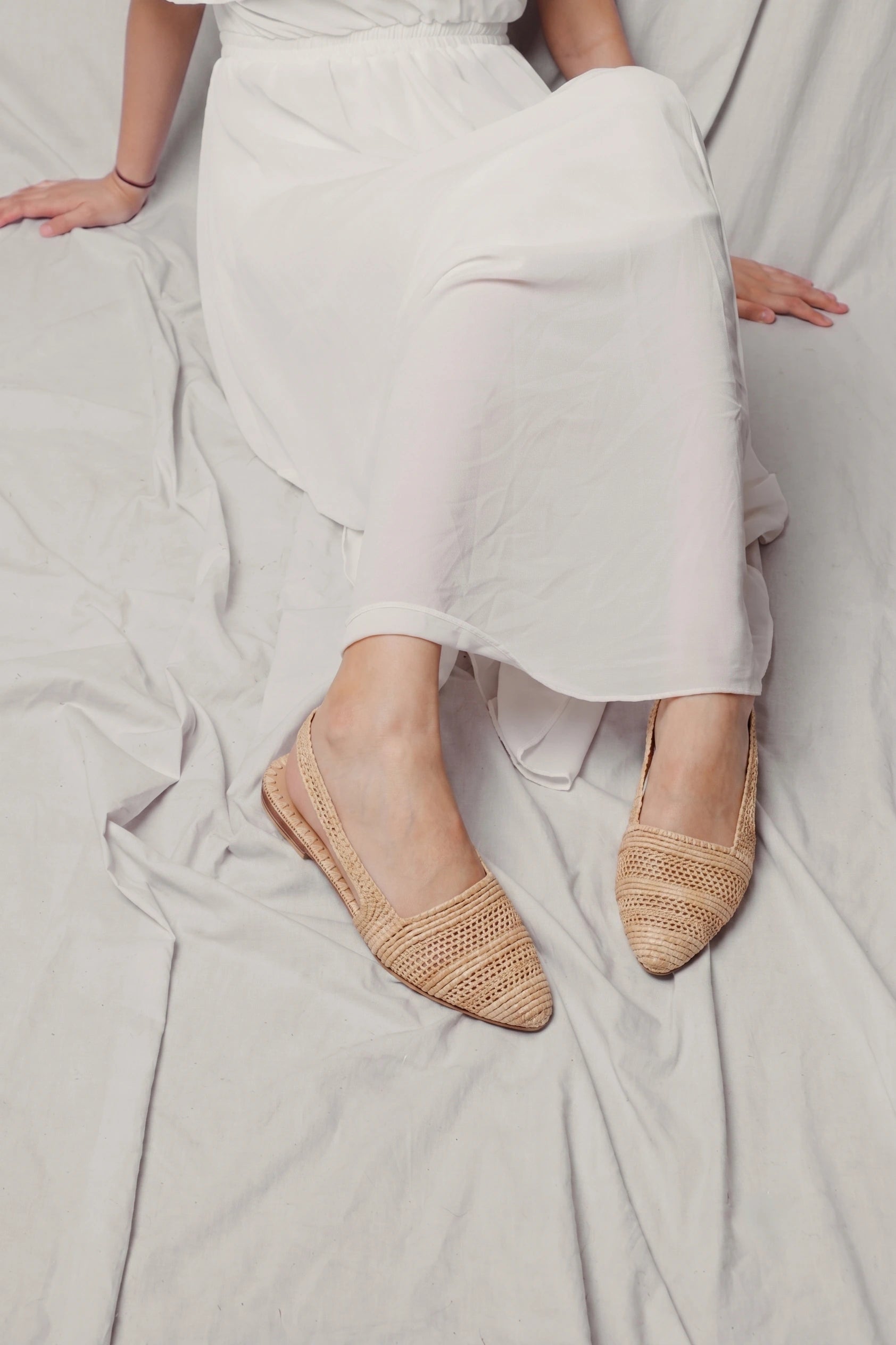 Seated model in white linen wearing Naima natural raffia slingback flats
