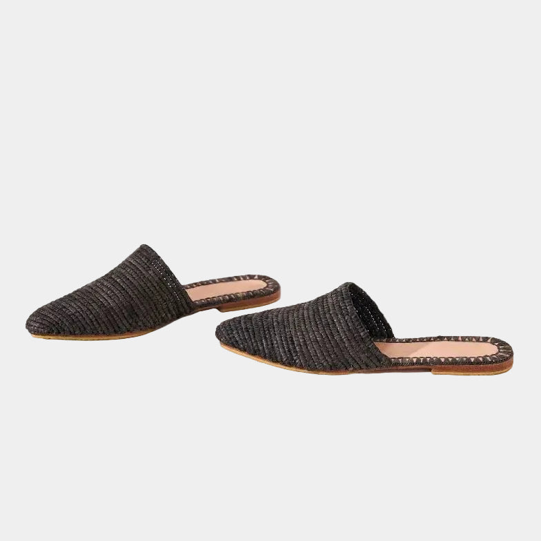 Black woven raffia babouche mules with leather soles on stone steps — Tilila mule by MARRAVIE