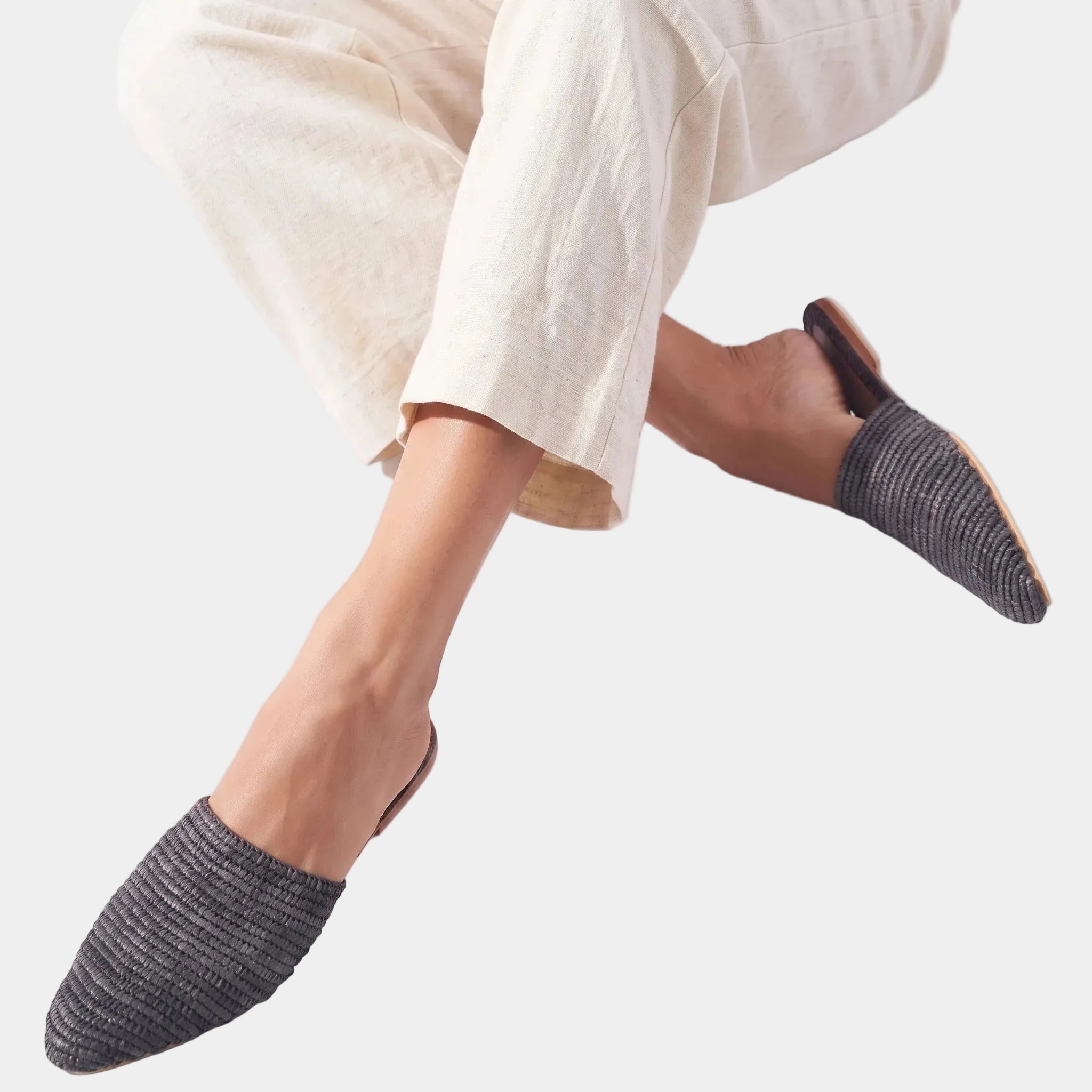 Woman with crossed legs wearing black raffia babouche mules — Tilila mule by MARRAVIE
