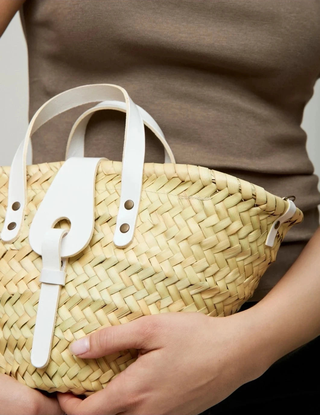 Woman holding the Zahira Mini palm leaf basket bag in white calfskin details