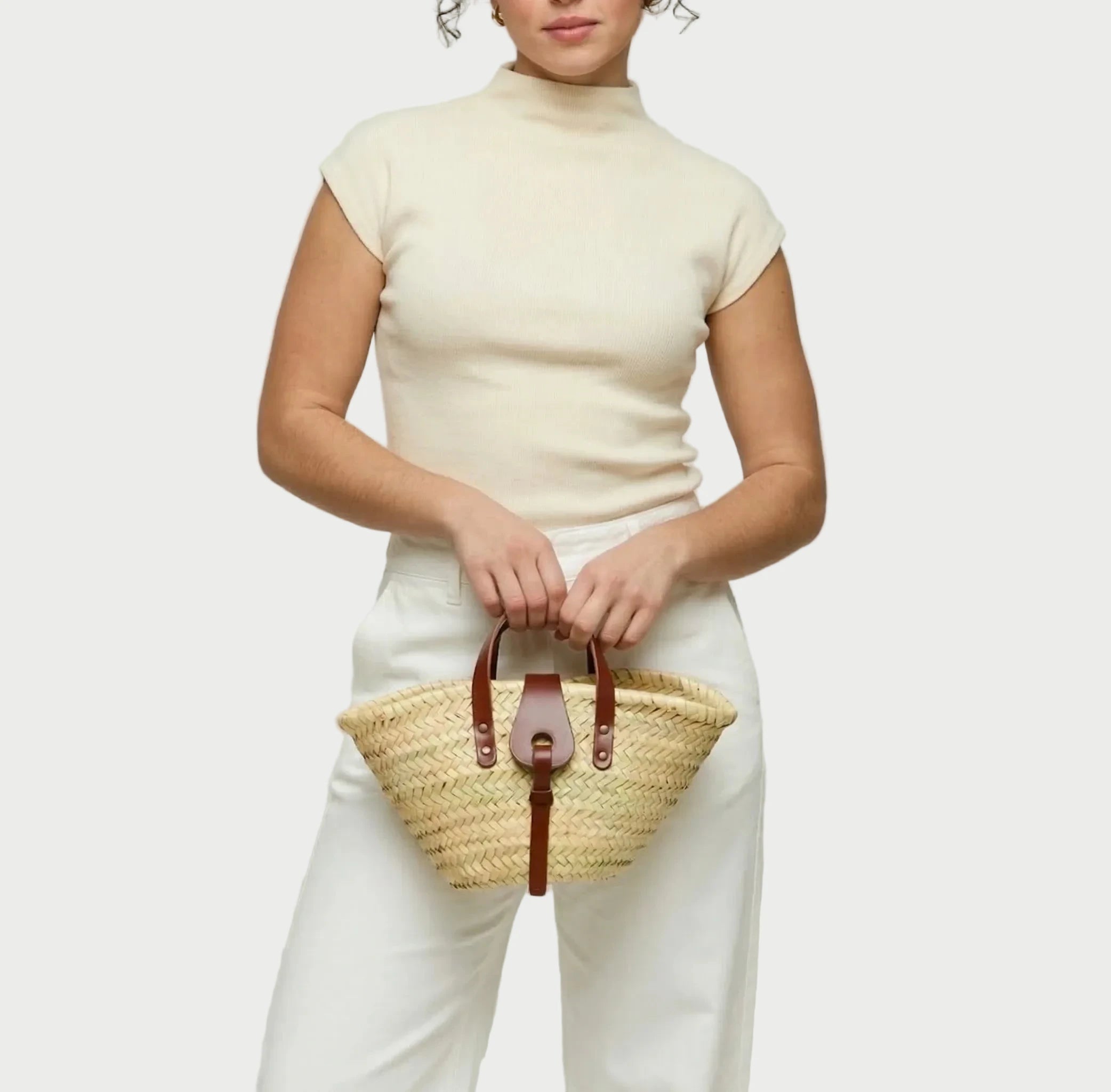 Woman holding the Zahira Mini palm leaf basket bag, styled with jeans and a silk top