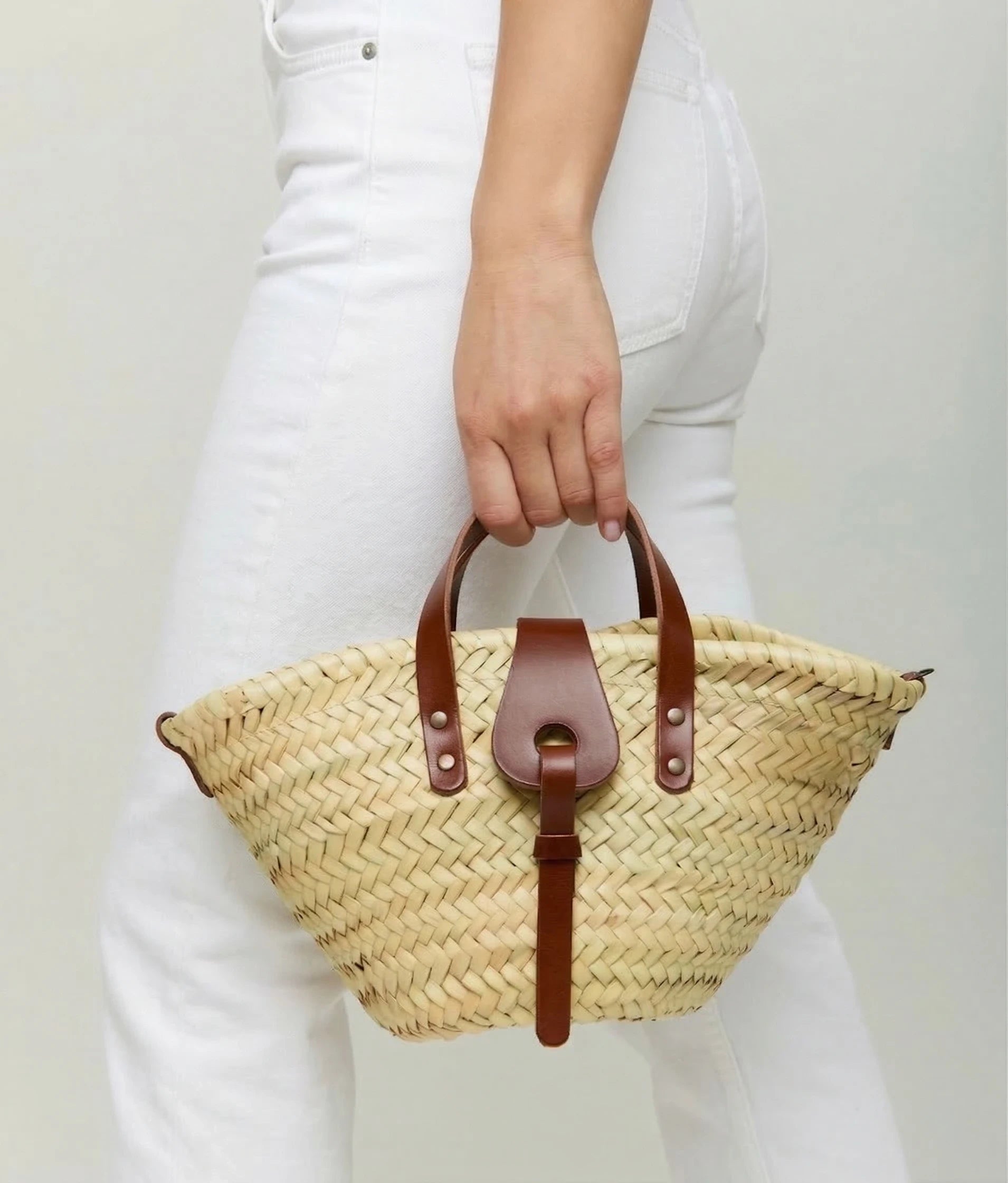 Woman holding the Zahira Mini palm leaf basket bag, styled with white jeans 