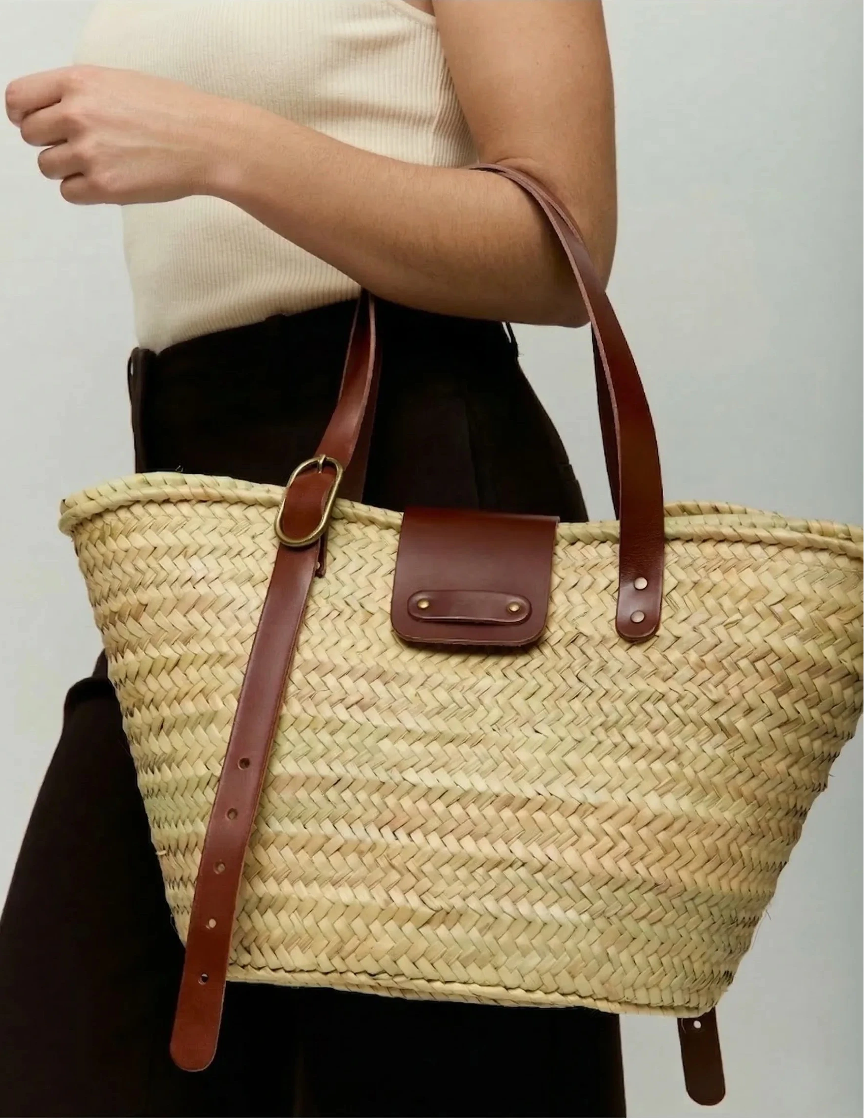 Woman carrying Aicha palm leaf basket bag with dark brown calfskin leather handles