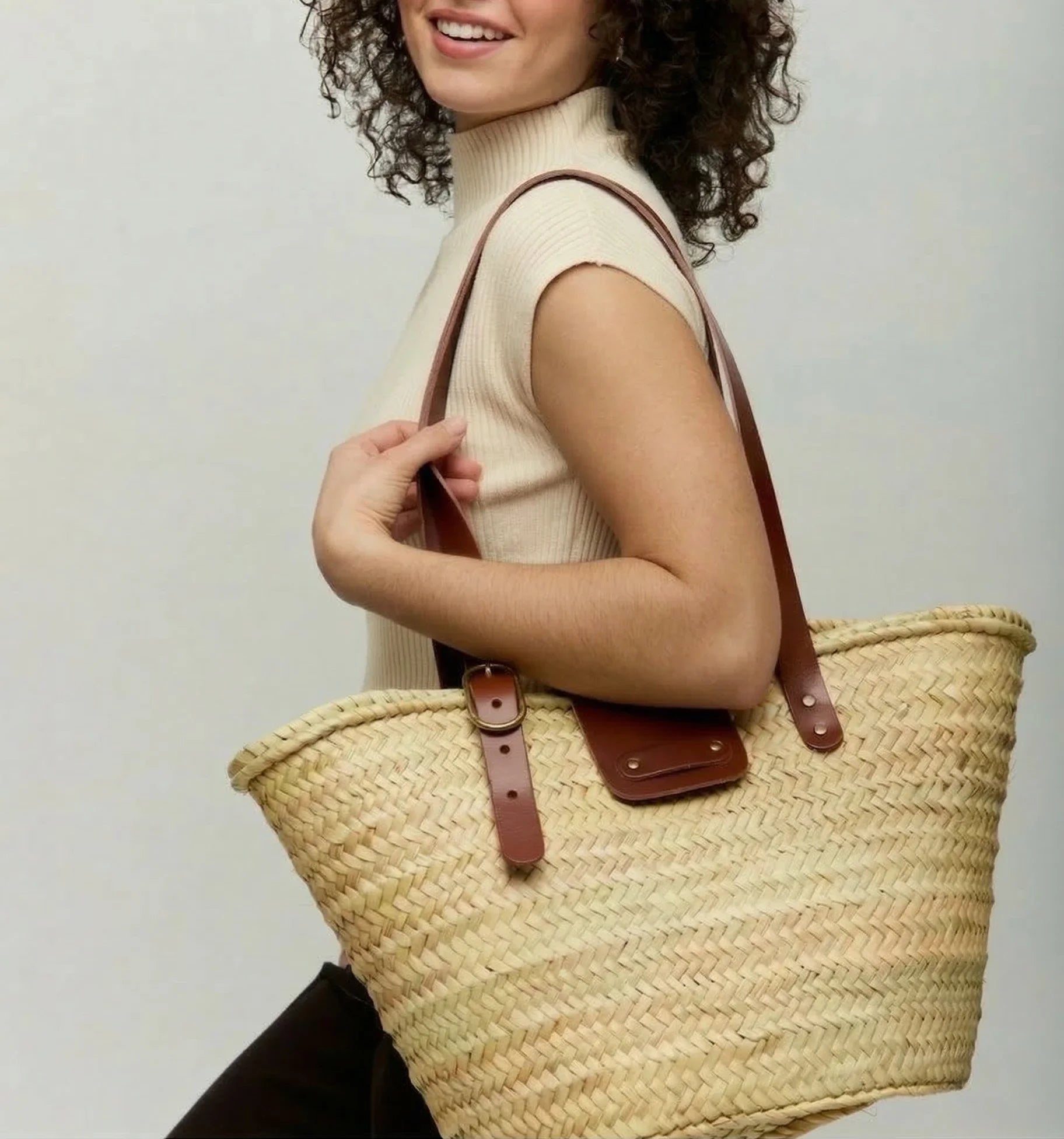 Model carrying Aicha palm leaf basket bag with dark brown calfskin leather handles