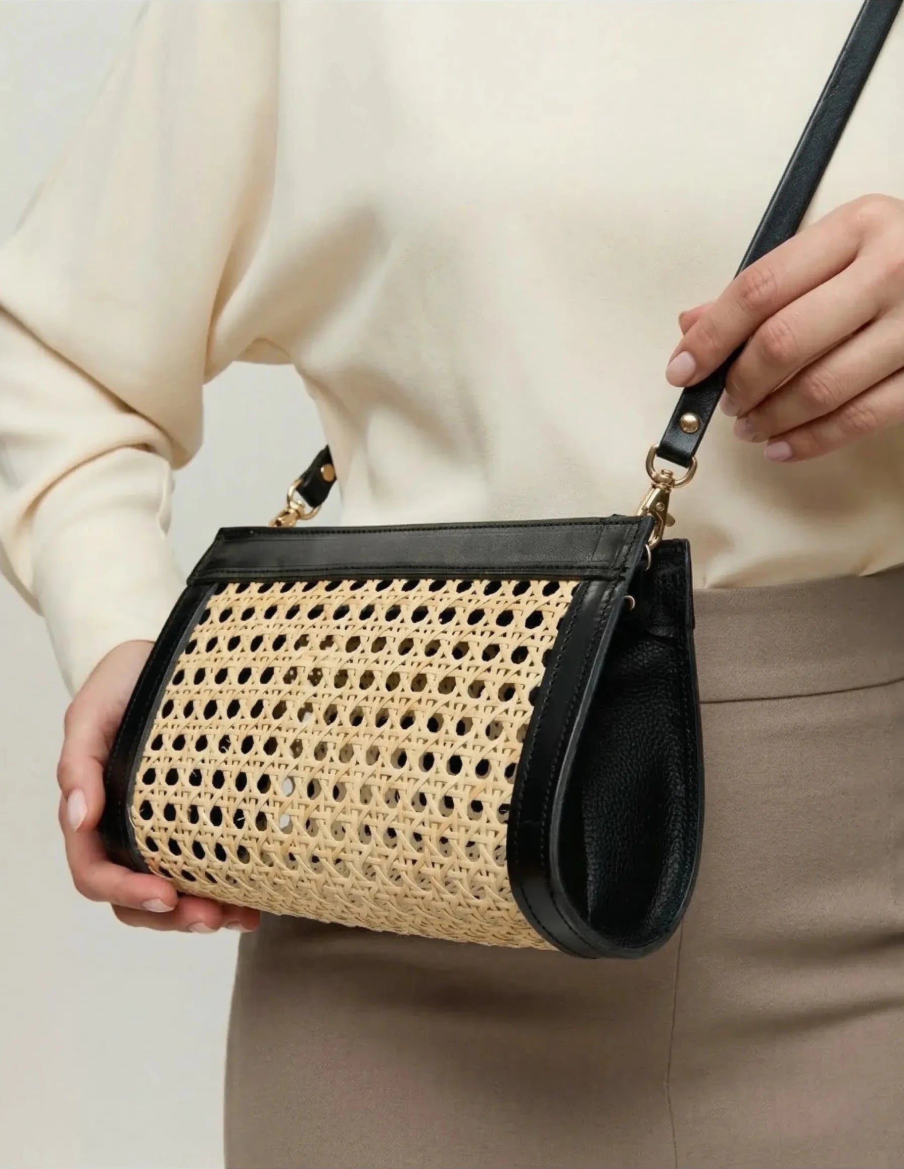 Model holding the Lamia rattan cane clutch by its crossbody strap