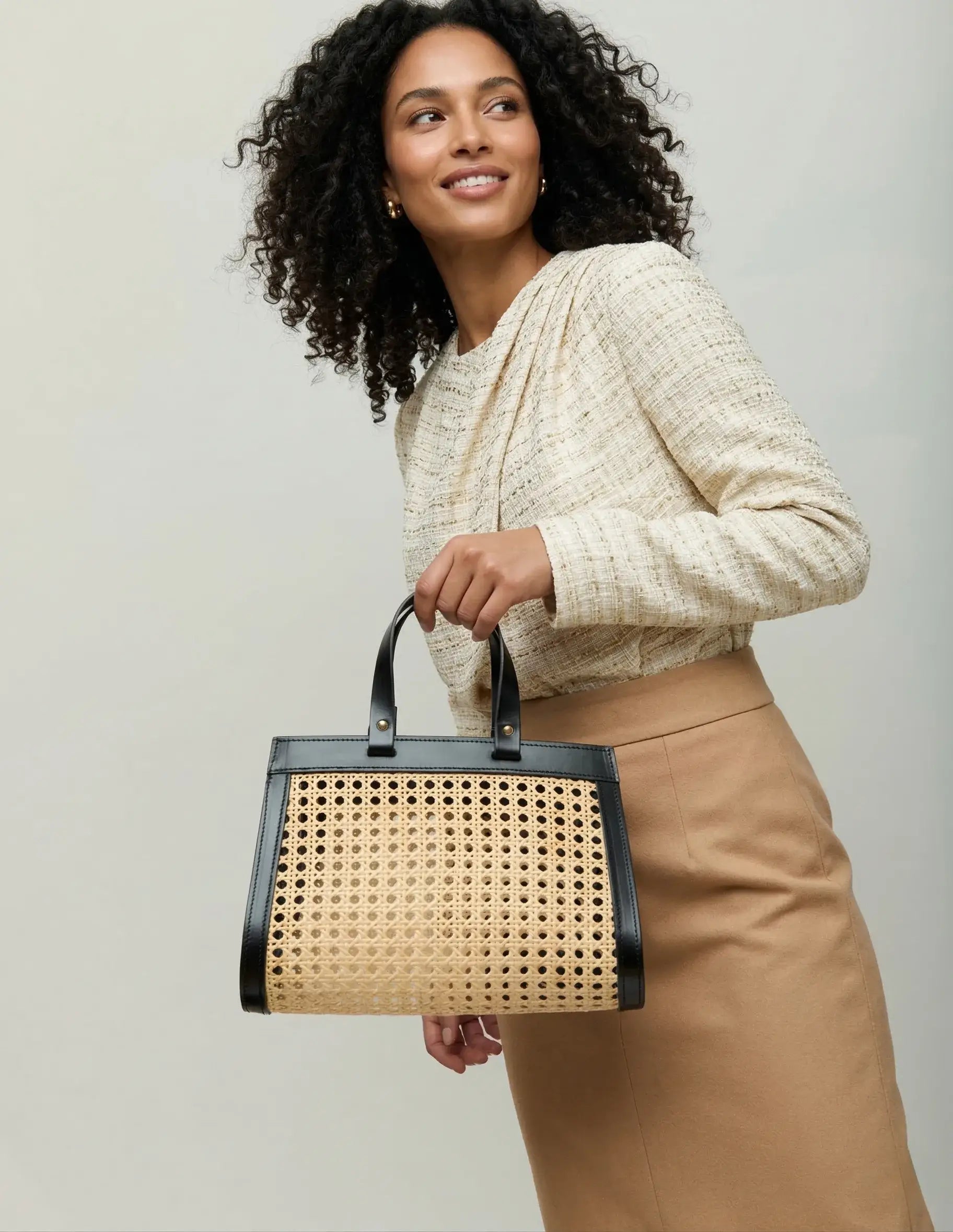 Lamia Mini Cane Bag carried by hand, shown with a cream knit and tan trousers