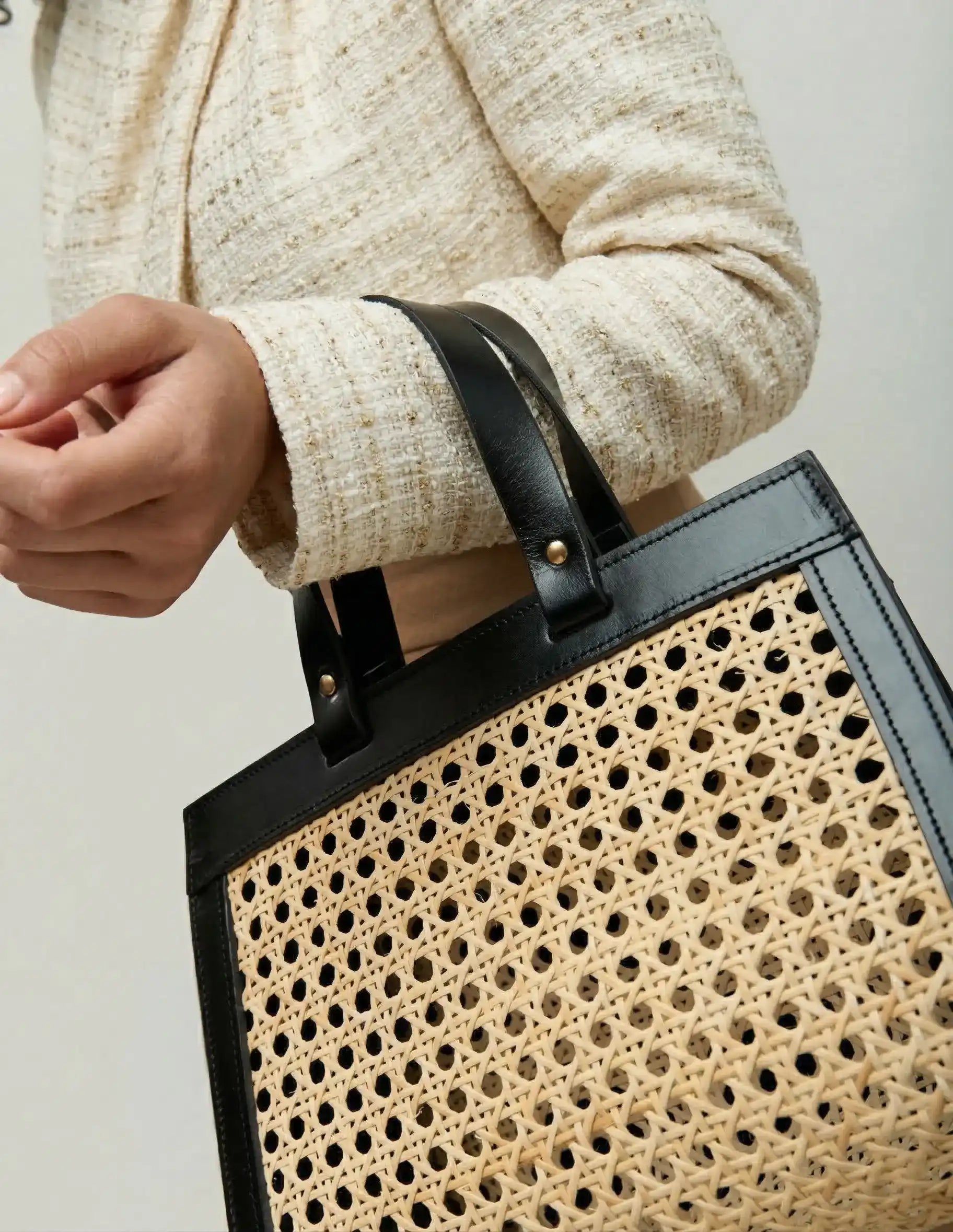 Model holding the Lamia Mini rattan cane bag by the top handles