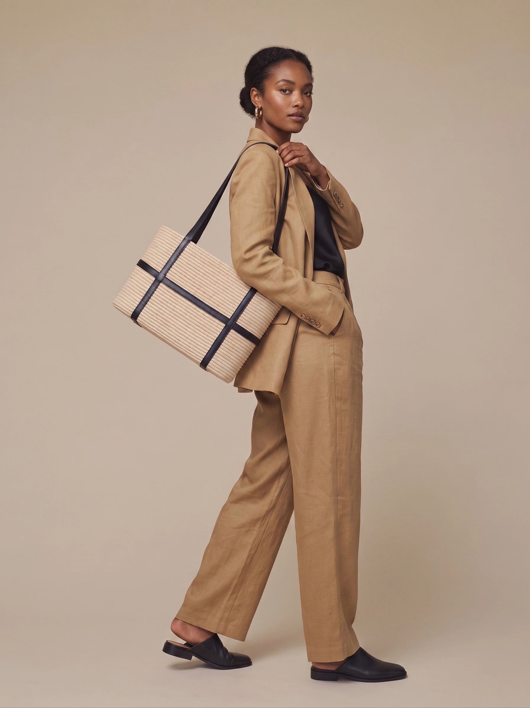 Woman in camel suit carrying Kenza structured raffia tote with black leather straps on shoulder