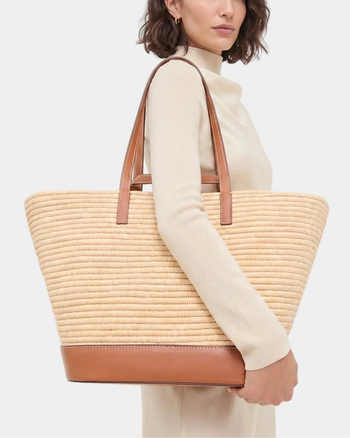 Woman in cream carrying the Najwa raffia basket tote on her shoulder.