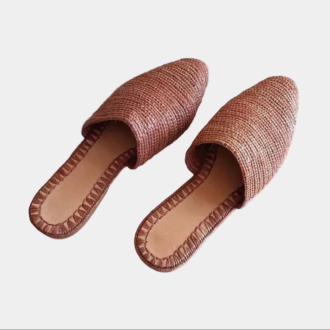 A pair of woven straw mule sandals in a warm terracotta brown color, displayed on a clean white background.