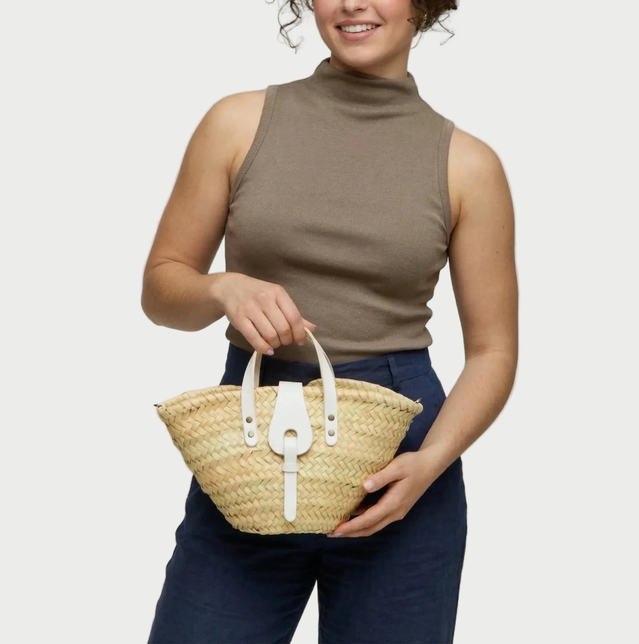 Woman holding the Zahira Mini palm leaf basket bag in white calfskin handles